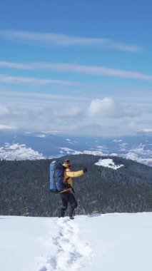 Büyük bir sırt çantası olan bir insan bir dağdaki derin karların içinden geçer. Manzara geniştir, uzak tepeler ve mavi bir gökyüzü vardır. Dikey görüntüler