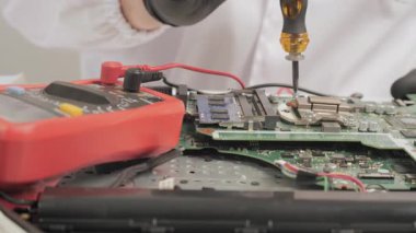 Kullanılan tornavida ve laboratuvar önlüğündeki teşhis cihazı kullanılarak devre kartını tamir eden, Aletler ve Çokölçer kullanan teknisyen ana kartı.