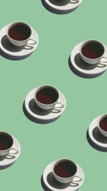 Seamless pattern of white cups with tea with strong shadows on a green background. Tea mugs move in different directions, vertical footage