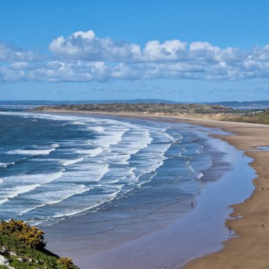 Galler 'deki Gower Yarımadası' nda bulunan nefes kesici Rhossili Körfezi Sahili 'ne hoş geldiniz. Uçsuz bucaksız altın kum ve gök mavisi sularıyla bu sahil doğanın kendisi tarafından yapılmış bir şaheser..