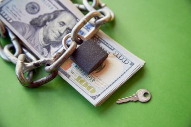 Bir zincir ve kapalı kilit, anahtarın yanındaki 100 dolarlık banknotların üzerinde duruyordu. Para kilitliyor, finansal kaynakları kilitliyor, hesapları donduruyordu.
