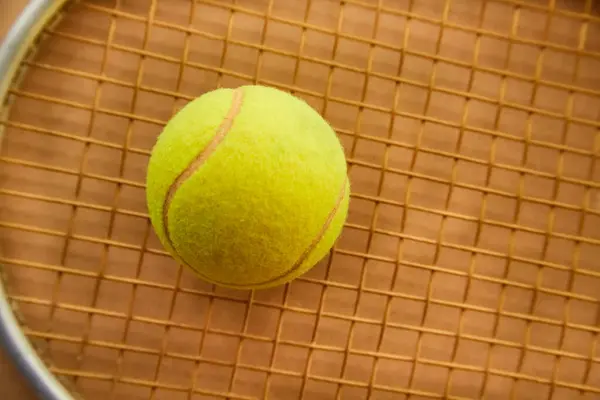 Tenis topu, kumlu bir arka planda raketin üzerinde uzanır. Yakın plan, kil tenis kortunda raketin üstünde bir top.