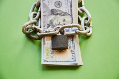 Üzerinde zincir olan yüz dolarlık banknotlar ve kapalı bir kilit, mali yardımı engelleme, fonları bloke etme, parayı bloke etme, banka hesaplarını engelleme.