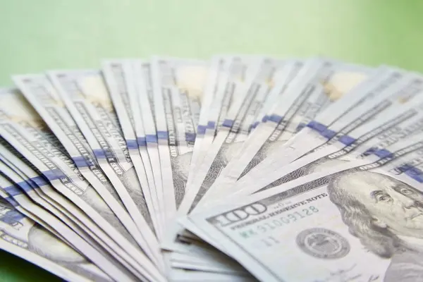 Yüz dolarlık banknotlar dikkatsizce yeşil arka plana saçılmış..