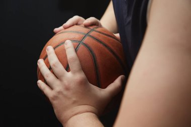 Basketbolcunun elleri topu kenarda tutar, basketbolda topu korur, basketbolda topu siyah arka planda koruma tekniği.