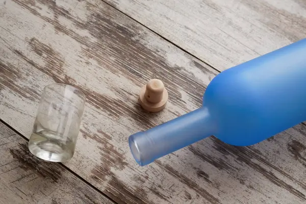 Boş votka şişesi masada, shot bardağı ve mantarın yanında.