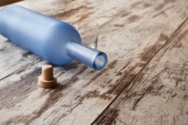 Boş mavi bir içki şişesi ve mantar yıpranmış ahşap bir masada yatıyor. Alkol sorunu, partinin sonu.,