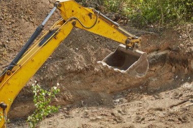 Kazı makinesinin kovası zemini kazıyor, kazıcının kovası kazı çukurunu kapatıyor, inşaat işi, çukur kazıyor.