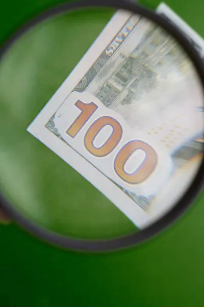 Bir büyüteç, 100 dolarlık banknottaki rakamı büyütür. Kârın artması, özgünlüğü kontrol edilmesi, banka mevduatının artması, dikey çekim, yakın çekim.