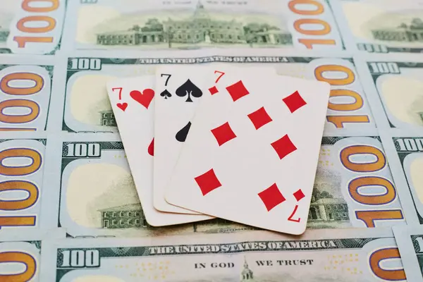 Bir deste iskambil kağıdından üç yedili 100 dolarlık banknotlara yayılmış, büyük kazanç, kumar, kumarhanede kumar...