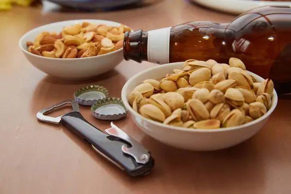 Bira kapakları için şişe açacağı ve masa üzerinde fındık tabakları, bira barı ve bira atıştırmalıkları olan boş bir bira şişesi.