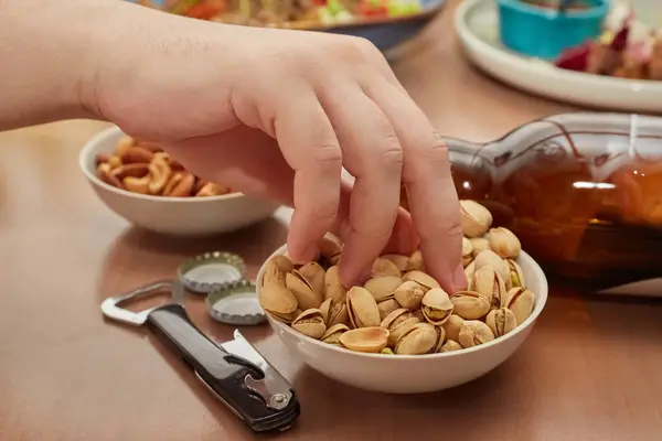 Bir el masanın üstündeki tabaktan şam fıstığı, şişe açacağı, ve boş bir bira şişesi, bira için atıştırmalıklar, barda bir masa alır.