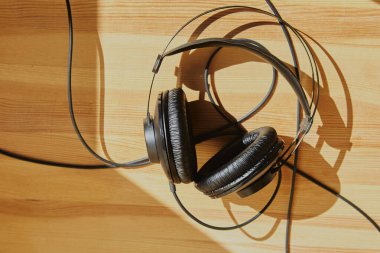 Güneş ışınlarındaki ahşap arka planda siyah kulaklıklar, güneş ışığındaki siyah kulaklıklar, ses toplama için arka plan, podcast için arka plan.
