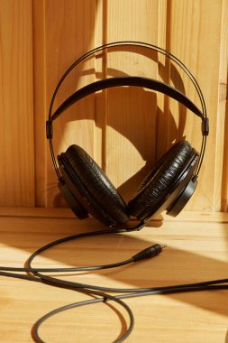 Güneş ışınlarında ahşap bir zemin üzerinde siyah kulaklıklar, podcast için arka plan, dikey çekim