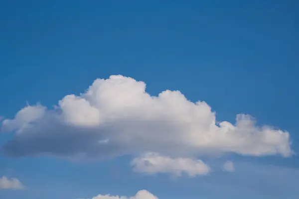 Mavi gökyüzünde beyaz bir bulut, güneş ışığıyla aydınlatılır, bulutlarla çevrili cennetsel bir manzaraya yakalanır.