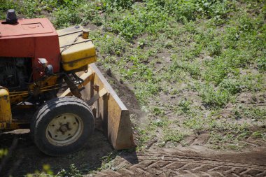 Buldozer çimlerden inşaat alanını temizliyor, traktör yeşil çimlerden inşaat alanını temizliyor.