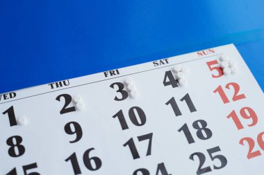 Takvimdeki beyaz haplar mavi arkaplanda, günlük ilaç dozunun artması, ilaçların dozajının artması, günlük yüksek dozda ilaç alması, ilaçların dozajının artması.