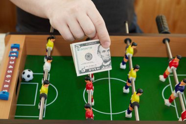Langırt masasının önünde 5 dolarlık bir banknot tutuyor. Spor, para oyunu, spor bahisleri, spor masası bahisleri. 