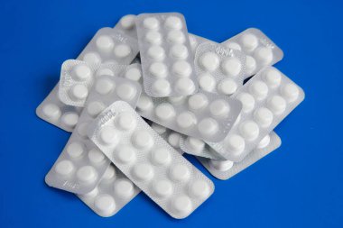 Mavi arka planda üst üste istiflenmiş beyaz tabletler, mavi arka planda beyaz haplar, yüksek dozda ilaçlar.