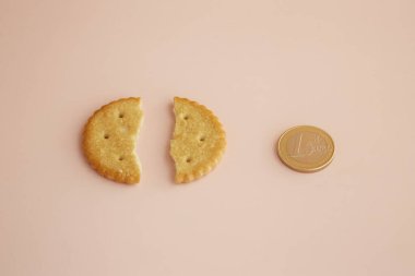Pembe arka planda ikiye bölünmüş bir kurabiye ve yanında da 1 Euro. Yakın plan, artan gıda fiyatları, yemek parası, bahşiş.