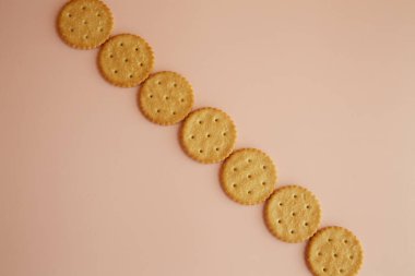 Pembe masa arkasında tek sıra halinde krakerler, taze pişmiş kurabiyeler, narin kurabiyeler.