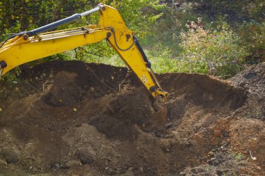 Kazıcının kovası toprağı delip geçiyor, büyük miktarda toprak kolayca hareket ediyor.