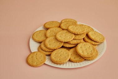 Pembe arka planda tuzlu krakerler, kağıt tabakta kurabiyeler, taze pişmiş kurabiyeler.