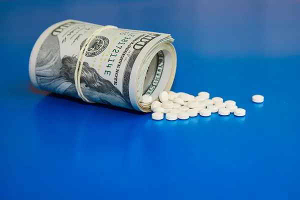Yuvarlanmış yüz dolarlık banknotlar, beyaz haplar masaya dökülüyor, tıbbi tedavi için para, pahalı ilaçlar, tarım ilaçları...