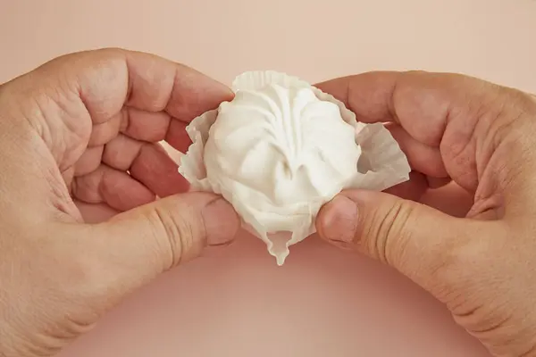 Elleri, beyaz bir turtanın içinde pembe bir zemin üzerinde lokum gibi bir kek tutuyor.