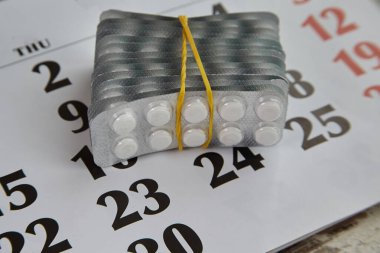 Kabarcıklarla dolu bir paket beyaz hap. Plastik bir bantla bağlanmış. Takvimde tarihler, yakın çekim, büyük miktarda ilaç ve uzun süreli bir hastalık var.