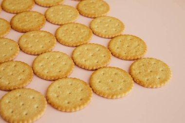 Pembe arka planda tuzlu krakerler, yakın planda kurabiyeler.