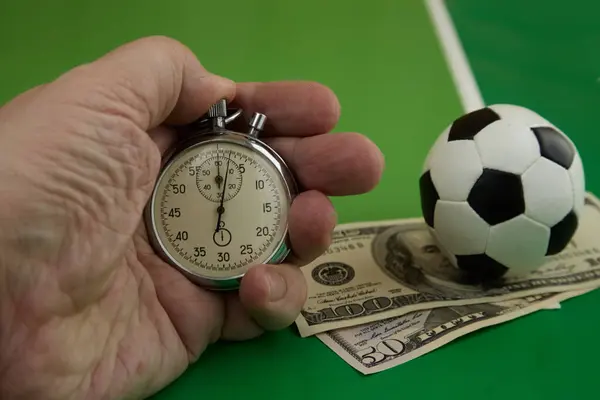 Kronometre elinde ve dolarla futbol topu yeşil arka planda, bahisçi oranları, bahis oranları, spor bahisleri, futbol posterleri, bahis zamanları