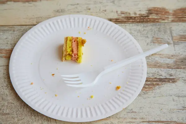 Arta kalan küçük bir parça sünger keki tek kullanımlık beyaz bir tabakta ve tek kullanımlık çatalla ahşap bir masada.