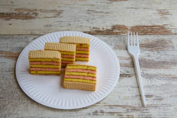 Tahta bir masanın üzerinde çatalla beyaz bir tabakta katmanlı sünger keki dilimleri.