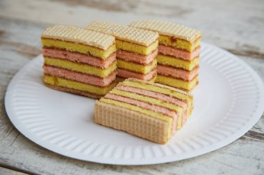 Sarı ve pembe katmanlı katmanlı sünger kek dilimleri ve ahşap bir masa üzerinde çatalla beyaz bir tabakta waffle.