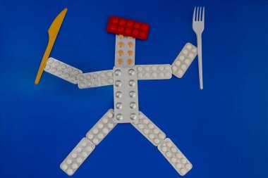 Mavi arka planda çatal ve bıçakla su toplayan haplardan oluşan insan figürü, vücut için vitaminler, düzgün beslenme ve diyet, yemek yerine hap.