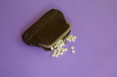 Leylak arkaplanındaki hapların madeni para yerine döküldüğü eski bir cüzdan, ilaç için para, tıbbi harcamalar, tedavi için para eksikliği.