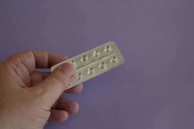 Leylak arka planında ilaç kapsülleri olan su toplayan bir el, ilaç parası, tıbbi masraflar.