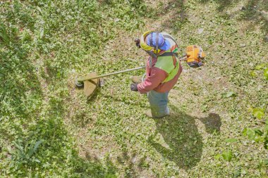 Çim biçme makinesi operatörü iş tulumuyla bahçedeki çimleri kesiyor..