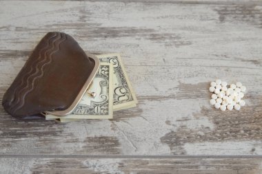 Dolarlarla dolu eski bir cüzdan ve yanında da aşınmış ahşap bir masa üzerinde bir avuç hap. Yakın plan, pahalı bir tedavi. Pahalı ilaçlar alıyor, ilaç alacak parası yok.
