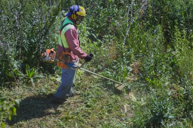 Tulumlu çim biçme makinesi operatörü ve çimenlikte çalışan bir kask..