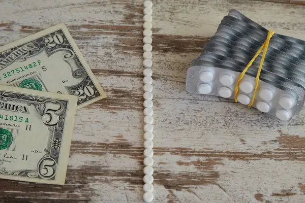 Bir beyaz tablet şeridi masayı ikiye böler, bir tarafta dolar ve bir paket uyuşturucu, tıbbi tedavi için sosyal güvenlik ödemeleri, pahalı ve ucuz uyuşturucular, uyuşturucu fiyatları