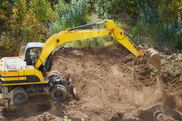 İnşaat alanının zeminini kazmaya çalışan kazıcı, inşaat sahasında kazıcı çalışması, yer hazırlığı ve toprak taşımacılığı.