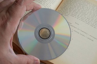 Arka planda metin, yakın plan, elektronik kütüphane, yeni ve eski teknolojiler, eğitim kursları olan açık bir kitaba karşı kompakt disk tutan bir el