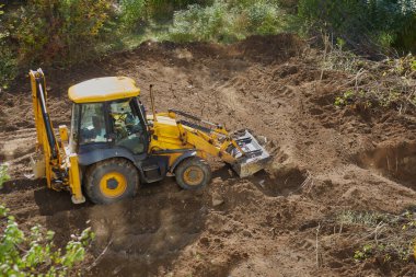 Buldozer yeşil ağaçların arasında bir inşaat sahasının zeminini dümdüz ediyor..