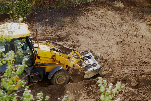 Buldozer yeşil ağaçların arasındaki inşaat sahasının zeminini düzleştiriyor, buldozer kirli bir alanda çalışıyor.