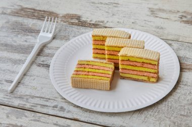 Beyaz tabakta katmanlı sünger keki, ahşap masada çatal, yakın plan meyve süngeri.