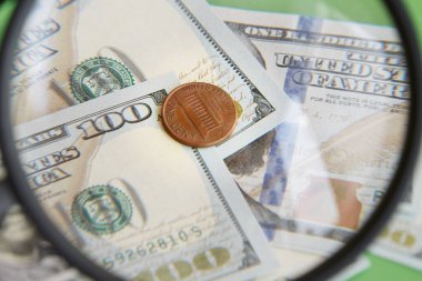 100 dolarlık banknotların arka planında yeşil arka plandaki büyüteçten geçen bir sent para, dolar başına bir sent, asgari kar.