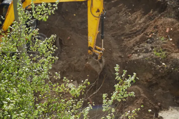 Çalışan bir kazıcı kovası ağaçların arasındaki inşaat alanını temizliyor 