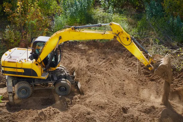 Kazıcı, zemini, zemini, zemini, altyapıyı, inşaat alanını ve mekanik yapıyı, siteprezasyon ve toprak hareketini yerle bir ederek, bir inşaat sahasının üzerindeki kovadan toprak döküyor.